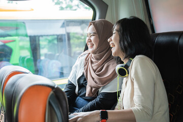 two young women laugh while chatting together while sitting on the bus