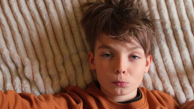 Portrait of preteen boy lying on soft blanket, warm colors. His hand gesturing NO sign at the camera, shakes head negatively turned left and right along to indicate disagreement, denial, rejection.