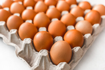 Raw chicken eggs in a cardboard tray with brown eggs, soft focus