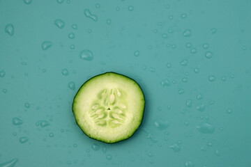 A small circle of fresh cucumber on a blue background with water drops. Low-calorie and watery vegetable. 