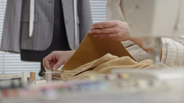 Hands woman dressmaker working in workshop chooses the color of the fabric. closeup, with tailoring mannequin, colorful clothes, fabrics and tools on the table in background