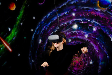 A young girl plays battles in a video game wearing VR virtual reality glasses. Space background, stars and planets