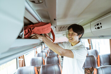 An Asian boy puts his bag on the shelf while standing on the bus
