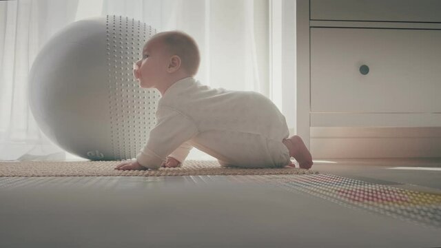 An interested baby with a pacifier crawls on the floor in front of the window