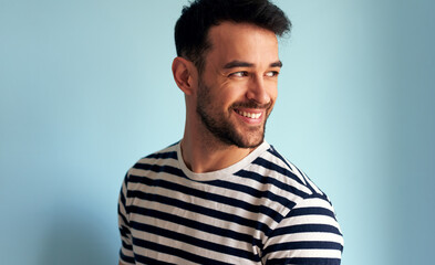 Joyful young man smiling, looking at one side, posing for advertisement, isolated on light blue background. Handsome male has joyful expression, posing against white blue wall.