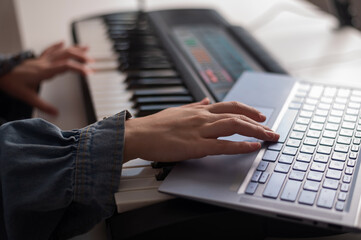 Close-up of female hands on the electric piano. A woman is learning to play the synthesizer on a laptop