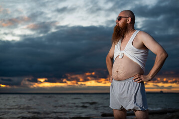 Humorous portrait of a brutal man posing on the beach at sunset