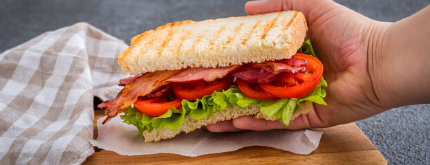 BLT sandwich with fried bacon, tomato and lettuce on a wooden board on a dark concrete background. American cuisine.