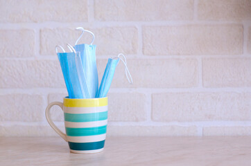 A blue-striped teacup with medical masks into it sits on the kitchen table against a white brick wall.