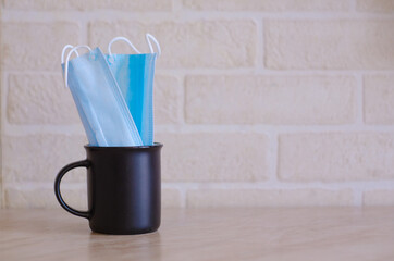 A black teacup with medical masks into it sits on the kitchen table against a white brick wall.