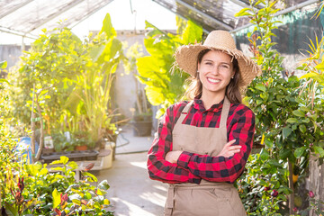 happy young woman with apron and straw hat in her greenhouse green business concept