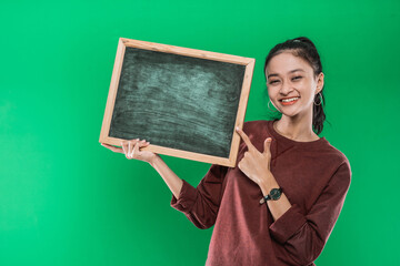 Young Asian woman presenting and pointing at something on a blank blackboard on a green background