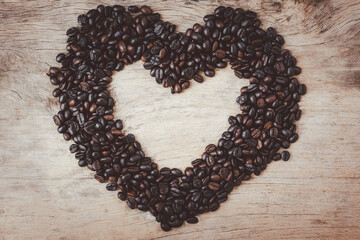 Big shape heart made from coffee beans on wooden table background.