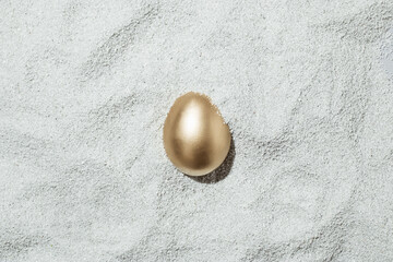 Fototapeta na wymiar A creative Easter concept with a golden egg covered in sand on the beach. Summer and holiday idea. Flat lay.
