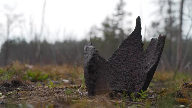 Rusty metal shell splinter lies in the forest in a war zone, it is raining and cloudy