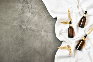 Brown bottles with pipettes and with ears of wheat, white towel on a grey concrete background. Copy...