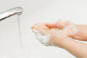 Elderly woman washes her hands with soap under the tap in the bathroom, the recommendation of frequent hand washing. Domestic hygiene