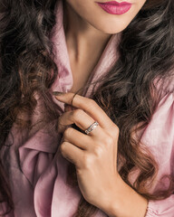 Elegant ring on the finger of a beautiful young woman straightening her long hair. Well-groomed skin of face and hands. Concept of fashion and style.
