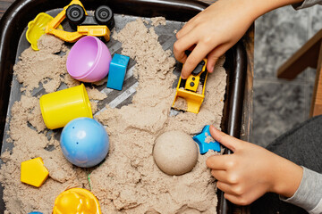 Child playing with kinetic sand and toy construction machinery. Hand of child in sand close up. Flat lay, top view. Indoor Table Game. Creativity Game concept. Activity for fine motor development. © Serenkonata