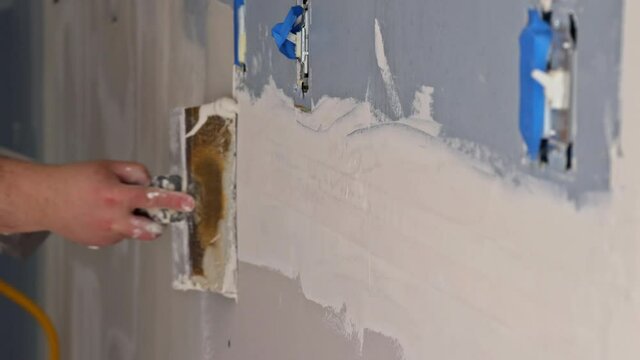 Worker working with putty and spatula work aligns with wall