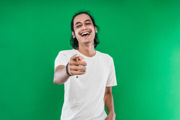 handsome man with long black hair Asian laughing happily while pointing at camera on a green background