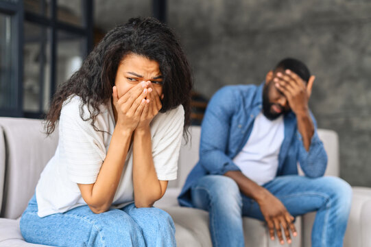 Young biracial couple relation problem concept, african woman feeling sad and crying after have an argument at home, sad or depressed woman sitting on sofa with her couple, man in defocus sits near