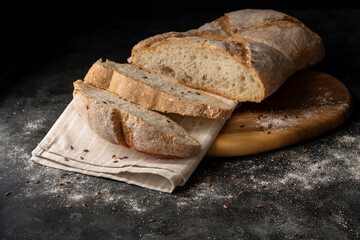 Slices of white bread are cut from a larger loaf on a wooden cutting board and dark background