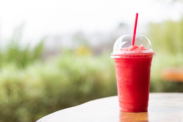 watermelon smoothie in take away cup placed on wooden table with natural blurry background