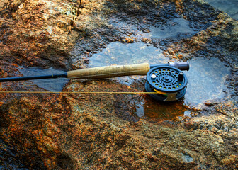 Taking a rest the fisherman placed the fly fishing rod and reel laying across the wet rocks at waters edge.