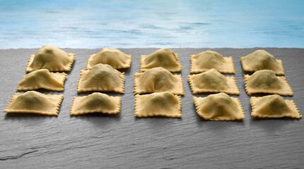 homemade ravioli without machine on black plate and blue background