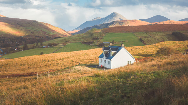 A lone traditional Scottish Highlands white croft house cottage in a rural mountain landscape countryside with Glamaig Peak and the Red Cuillins on the Isle of Skye, Scotland.