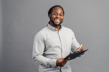 Cheerful African-American young man with dreadlocks holding a folder, taking notes, smiling black...