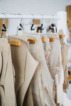 Many paper sewing patterns for different clothes hanging on the rack in sewing factory background. Clothing pattern, manufacture on sewing factory. Tailoring, small business