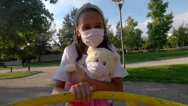 girl and her bear wearing mask rolling in public park toy