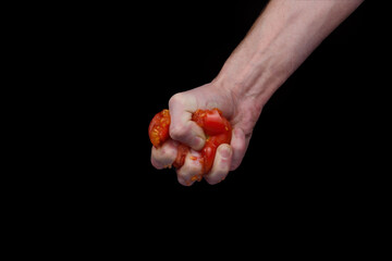 A man's hand crushes a red tomato on a black background.