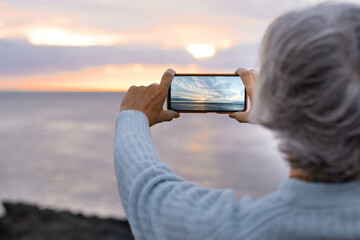 Close-up of woman hands photographing seascape and sunset with mobile phone