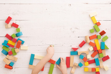 Top view of child's hands playing with colorful wooden bricks on white wooden table. Learning and education concept.