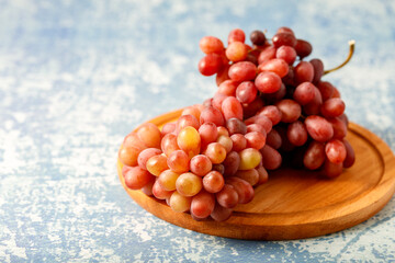 Large bunch fresh pink red grapes on wooden board on blue background.