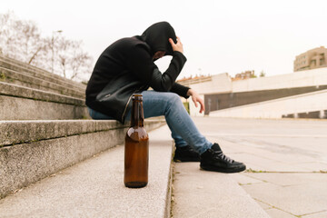 Close-up of a beer bottle on the floor with a drunk young man crying having problems and feeling stress. Youth social problem concept.