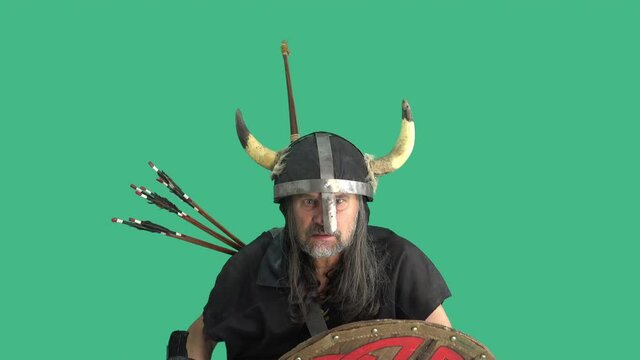 Mature viking in helmet with wooden shield emotionally swears and threatens his enemies with battle ax on green background