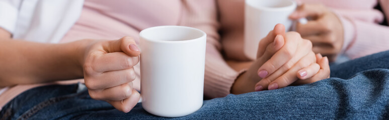 cropped view of girlfriends holding cups of tea in living room, banner