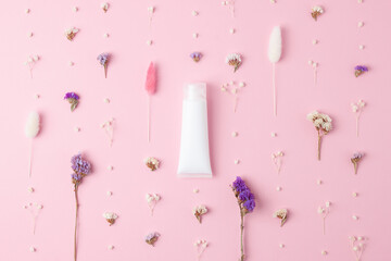 White tube of cosmetic cream with flowers on pink background. Flat lay
