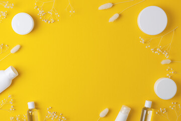 Cosmetic background with skin care products and flowers on yellow. Flat lay, copy space