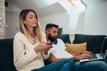 Couple using a smartphone and a laptop at home