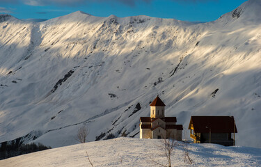 church with small house in high snowy mountains in evening light 