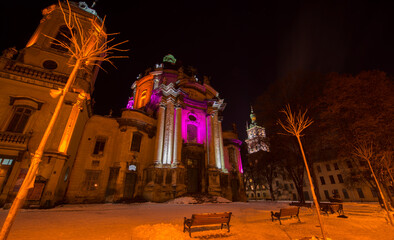 Night View of old basilica building in Lviv city with colourful backlight and snow on the ground 