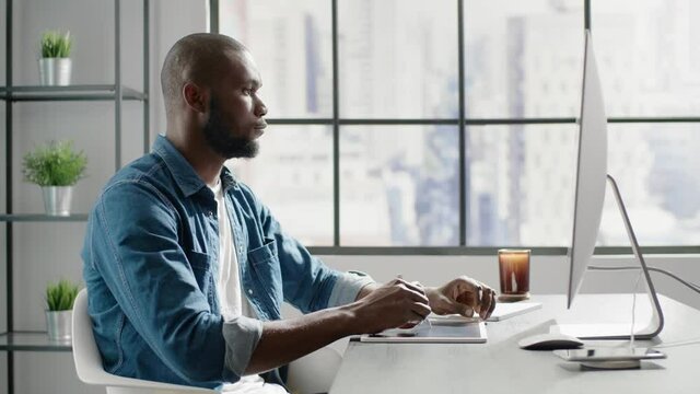 Afro-american freelancer in denim shirt makes mark on tablet