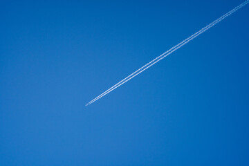 Airplane in flight with contrails in a clear blue sky