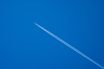 Airplane in flight with contrails in a clear blue sky