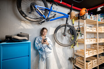 Portrait of a young handywoman standing relaxed with phone in the well equipped workshop or garage....